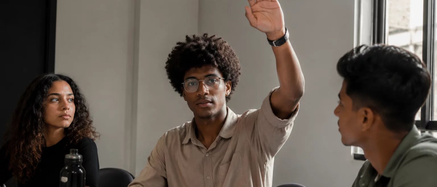 Participante com a mão erguida pedindo a vez, à mesa coberta de folhas escritas